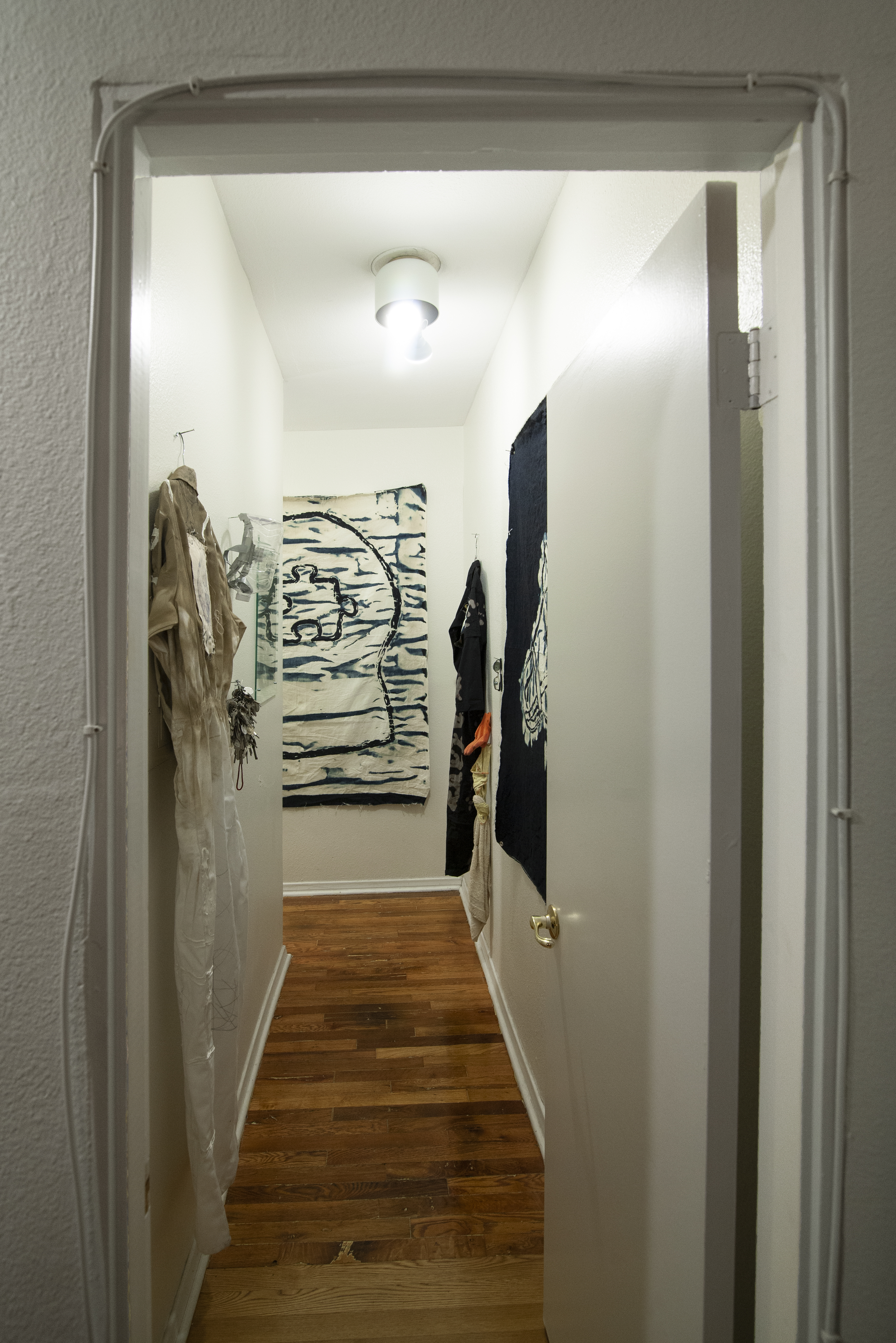 A narrow white hallway with clothing and art works hung on the walls